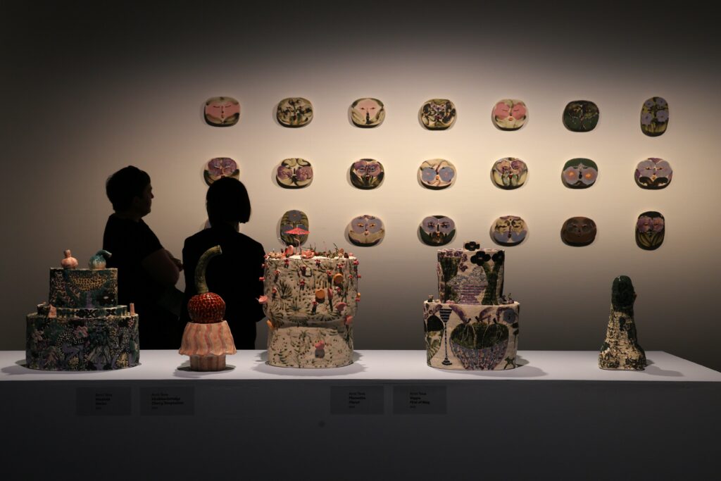 Kuva Kuopion taidemuseosta. Edessä näkyy taideteoksia ja kaksi ihmistä katselevat tässä uutisessa mainittuja teoksia seinällä.