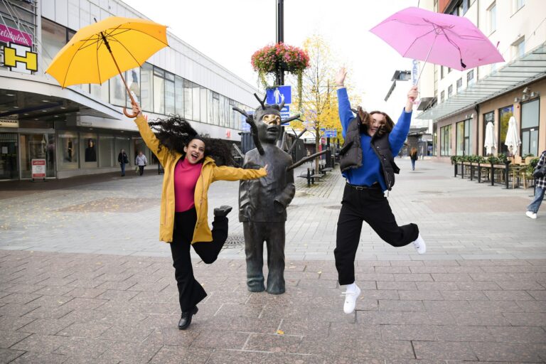 Kaksi nuorta hyppää ilmaan värikkäiden sateenvarjojen kanssa.