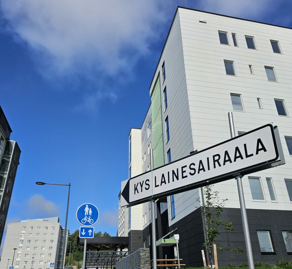 Kuva ulkoa Lainesairaalan edestä, etualalla liikennemerkki, jossa lukee Kys Lainesairaala.