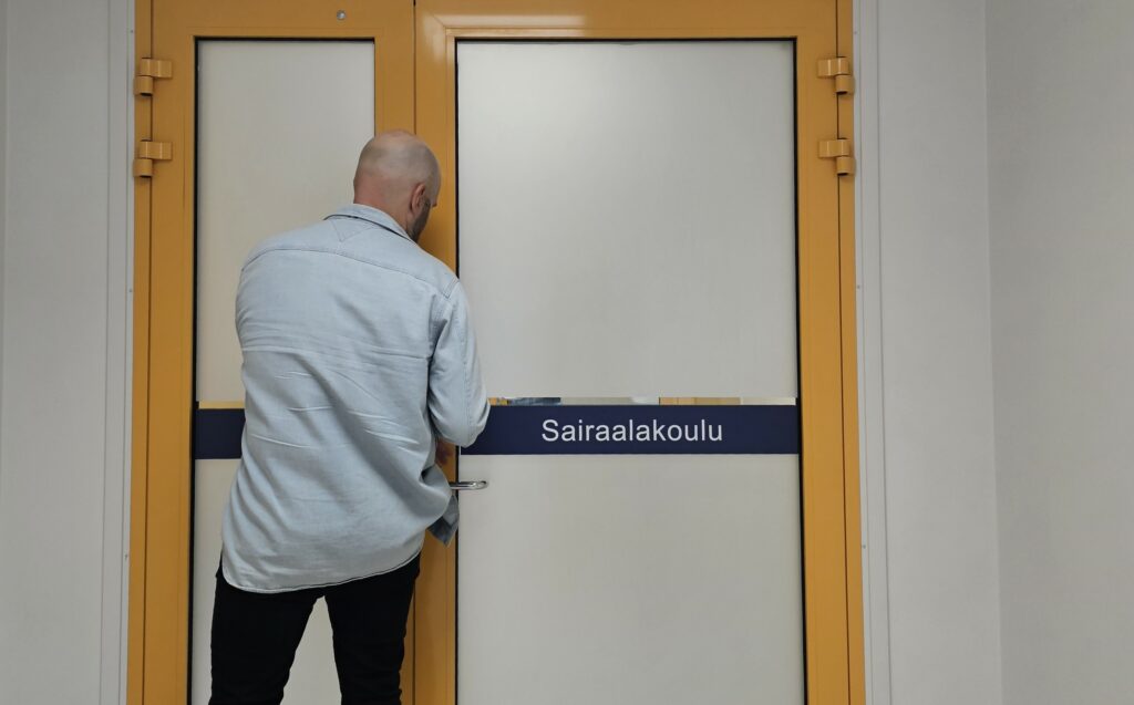 Kuvassa sairaalakoulun ovi ja opettaja avaamassa sitä.