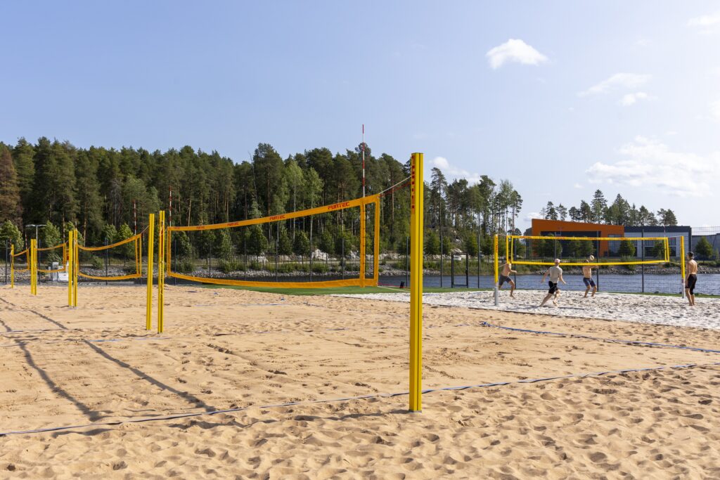 Beach volley -kentistä kuva, jossa pelaajia sivuttain oikealla olevalla kentällä. Taustalla näkyy Saaristokatu, oikealla myös järvenranta.