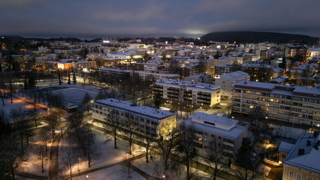 Iltahämärässä näkyviä rakennuksia valaistuksineen kaupungin keskustassa, ilmasta kuvattuna.