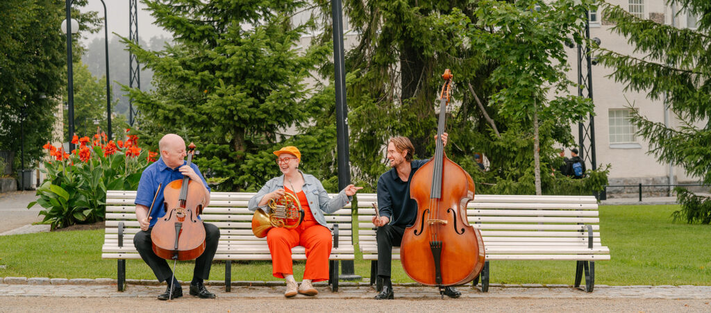 Orkesterin kolme muusikkoa puiston penkillä.
