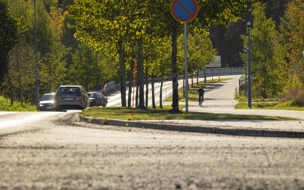 Kadulla ajaa kolme autoa, vieressä pyörätie ja jalkakäytävä. Teiden reunalla puita, joissa vihreät lehdet.