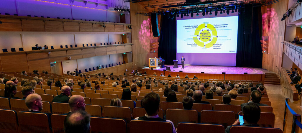 Musiikkikeskuksen Konserttisalin katsomossa yleisöä ja valkokankaalle projisoitu kuva.