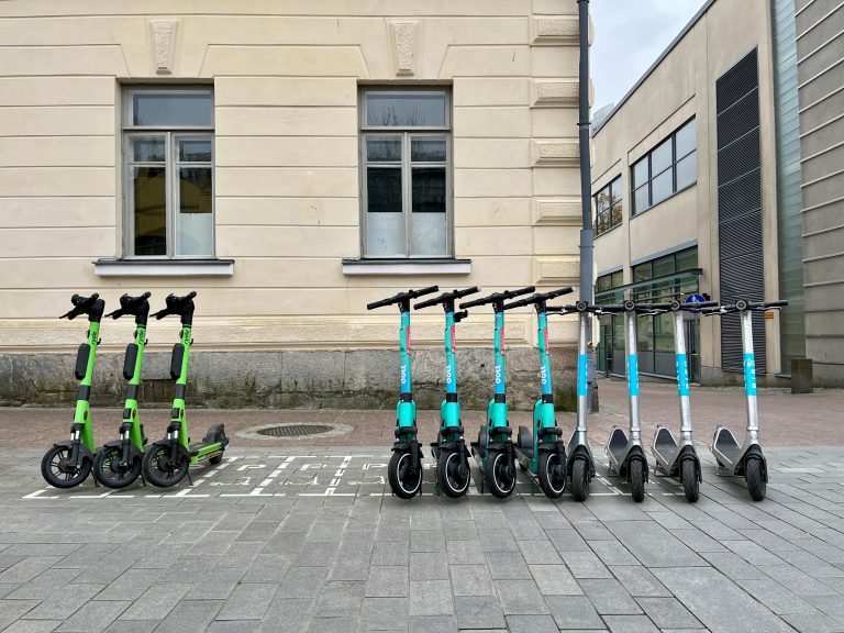 Sähköpotkulautoja siistissä rivissä niiden pysäköintiruuduissaan.