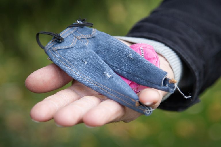 Pieniä vaatteita ojennetulla kädellä. Ympärillä luontoa.