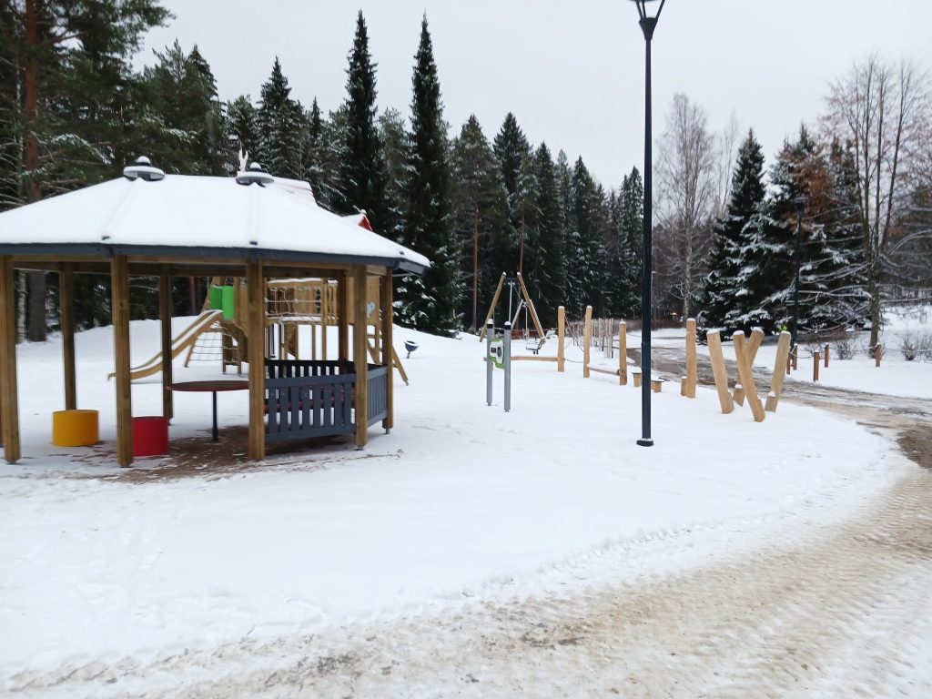 Talvinen leikkipuisto, jossa katoksella varustettu rakennelma, taustalla puita.
