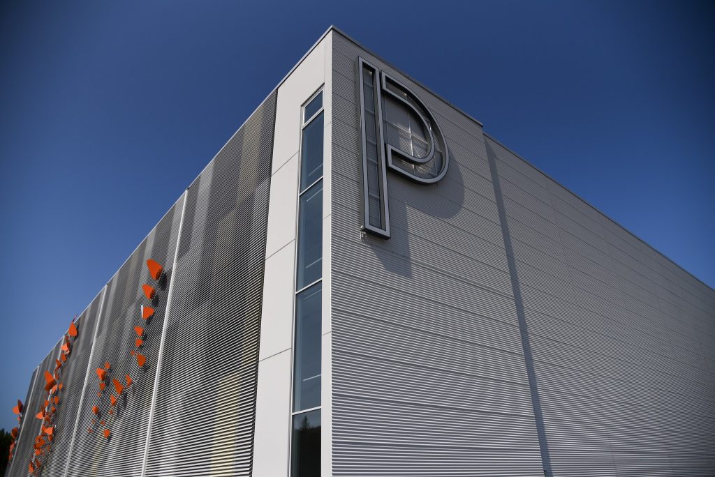 Pilvetöntä taivasta vasten kuvattua Sarastuskaaren pysäköintilaitoksen julkisivua, jossa oranssina hehkuva taideteos.