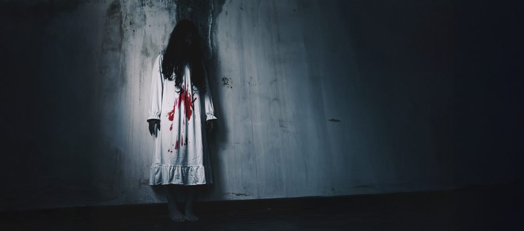 Naishahmo, jolla on verta vaatteissa, taustalla likainen seinä.