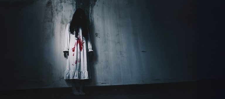 Naishahmo, jolla on verta vaatteissa, taustalla likainen seinä.