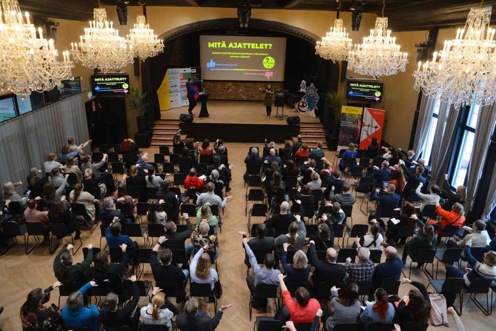 Suuri sali, jossa kristalliset kattokruunut, tuoleilla istuu lähes 200 ihmistä.