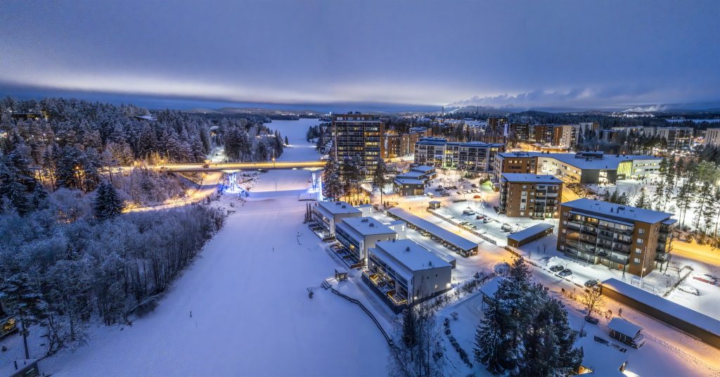 Pilvinen iltahämärä talvella, luminen Keilankannan kanava, jonka oikealla puolella iltavalaistuksessa olevia rakennuksia.