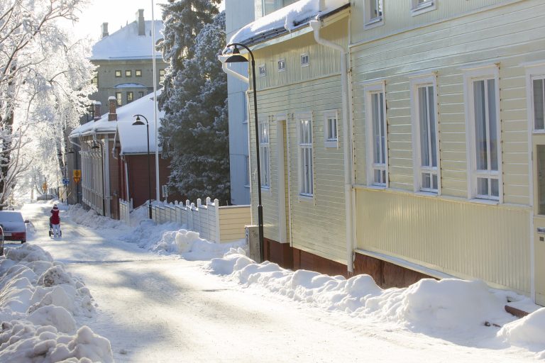 Talvinen katu, jonka oikeassa reunassa vaalean keltainen puutalo.