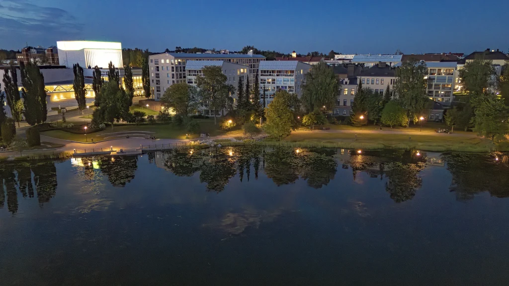 Lampi iltahämärässä, jonka taustala vihreitä puita ja kerrostaloja.