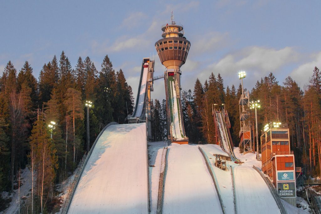 Puijon kolme hyppyrimäkeä talvisessa maisemassa, taustalla Puijon torni ja metsää.