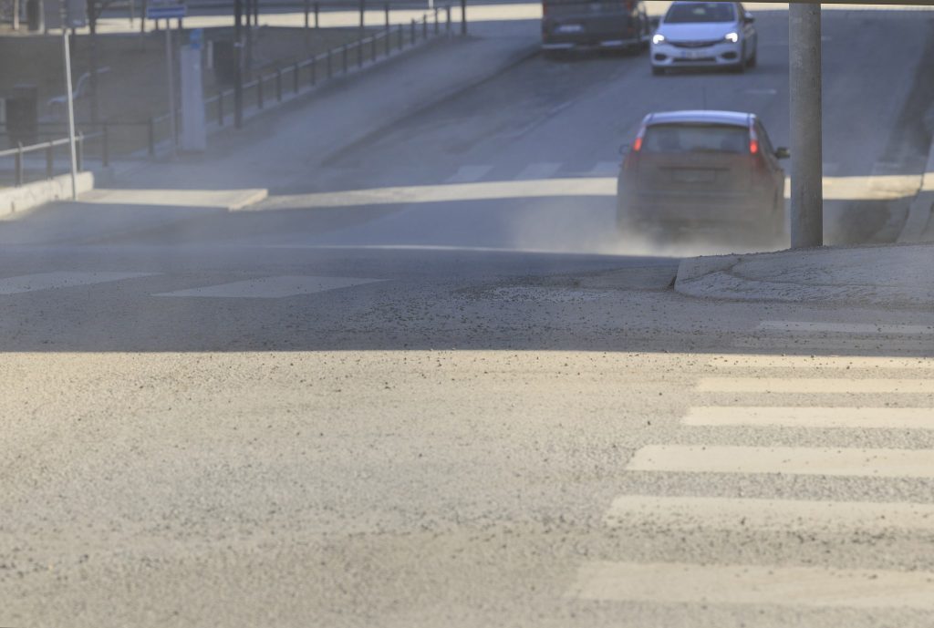Pölyävä hiekkainen katu ja suojatie. Kadulla ajaa kolme autoa.