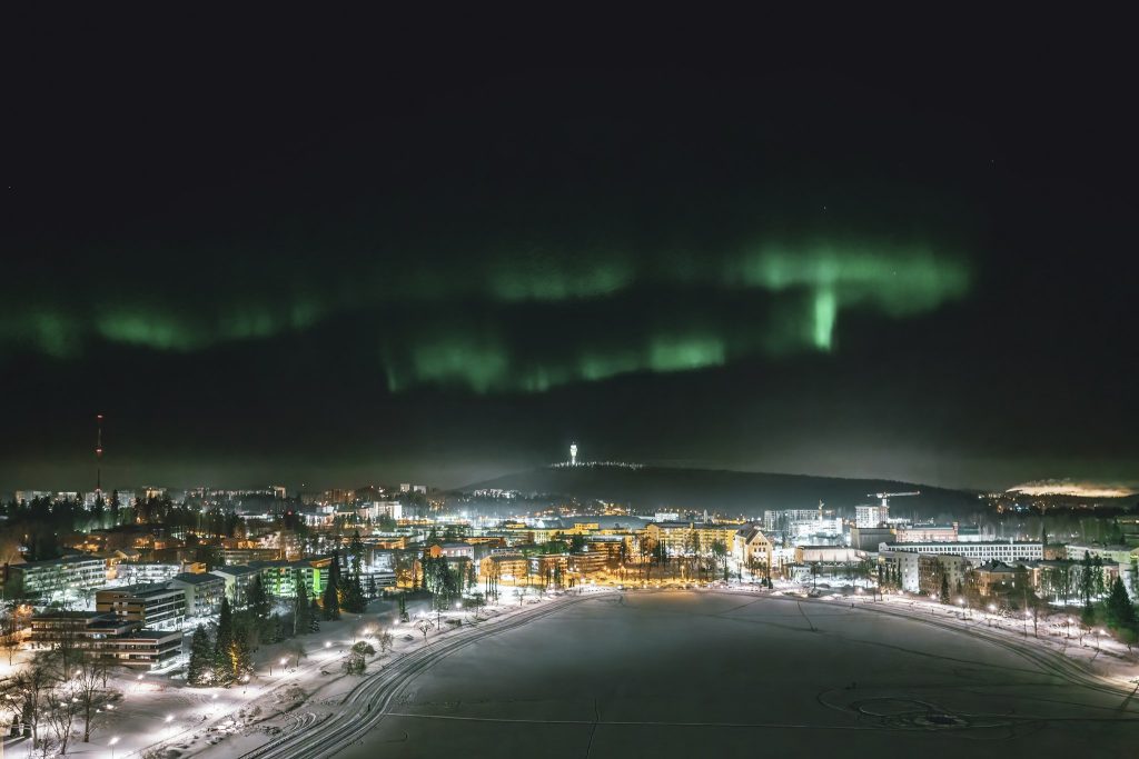 Tummalla taivaalla vihreitä revontulia kaupungin yllä.