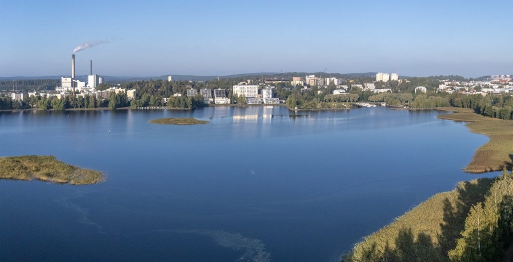 Järvimaisema, jossa taustalla kaupungin rakennuksia ja sininen taivas.