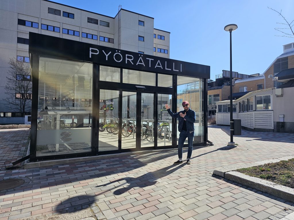 Kuopion pyörätalli aurinkoisessa säässä, etualalla hymyileväinen henkilö tallin edustalla.