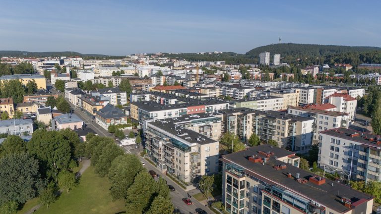 Kesäinen päivä, vihreitä puita ja rakennuksia, taustalla sininen taivas.