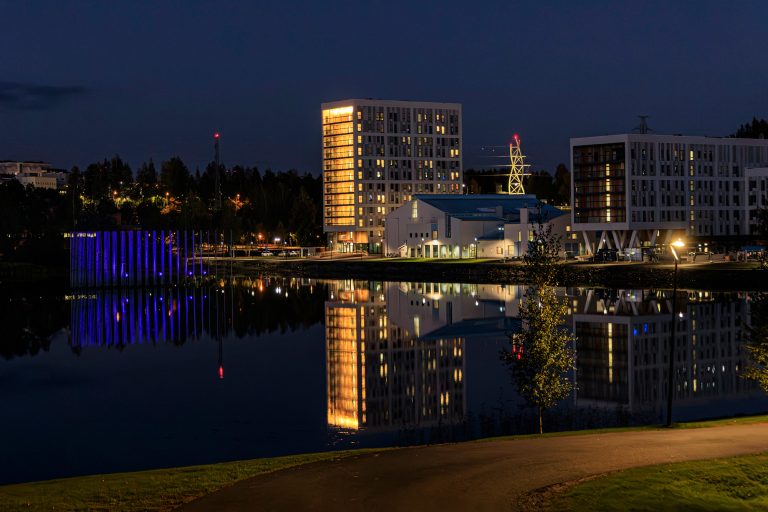 Rakennuksia järven rannalla iltavalaistuksessaan.