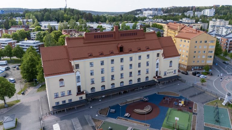 Vaalea monikerroksinen rakennus, jonka takana puita ja taloja.
