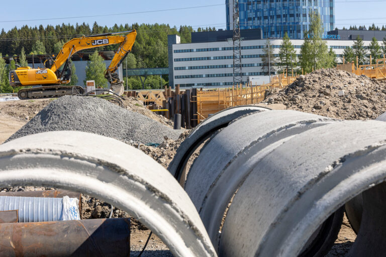 Kaivinkone työskentelee siltatyömaalla. Etualalla suuria betonielementtejä.