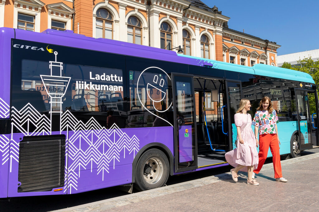 Kaksi naista nousee bussista kaupungintalon edustalla. Bussi on sähköbussi ja sen kyljessä lukee ladattu liikkumaan.