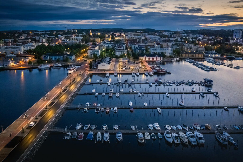 Satama iltavalaistuksessaan: Kallavesi, veneitä ja taustalla siintävät kaupunginvalot.