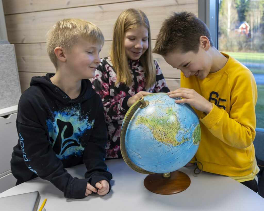 Kolme oppilasta tutkii karttapalloa.