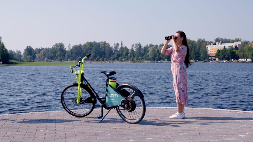 Nainen rannassa kiikareiden ja polkupyörän kanssa