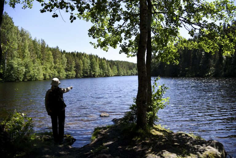 Nainen seisoo pienen kesäisen lammen rannalla.