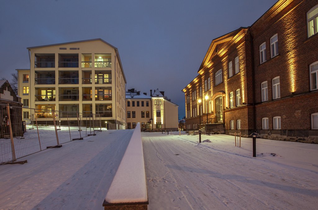 Kuva talvisesta kaupunkipihasta jonka taustalla on lämpimästi valaistuja kaupunkikerrostaloja