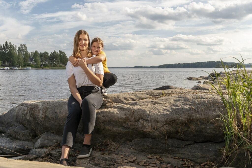 nainen ja lapsi istuvat kivellä järven rannalla.
