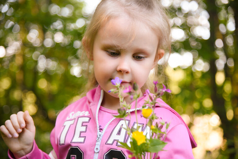 Pinkkihupparinen tyttö metsässä nuuhkii luonnonkukista poimittua kukkakimppua.