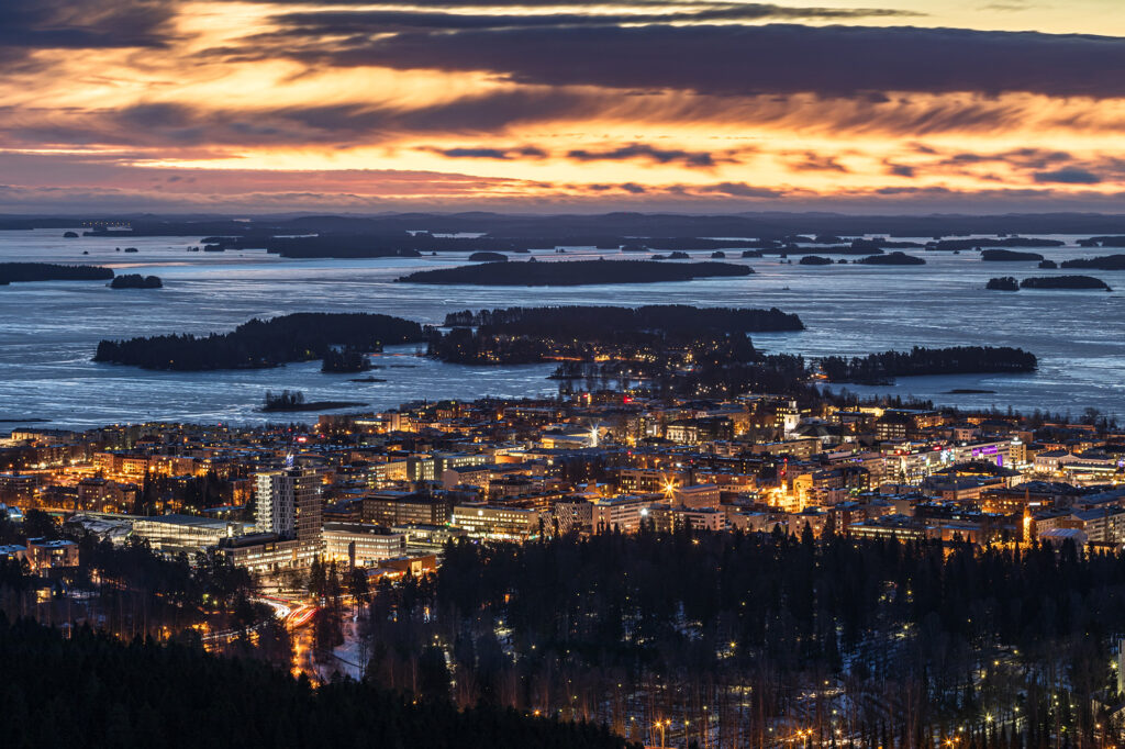 Kaupungin valot, järvi ja monivärinen taivas illlalla juuri auringon laskettua.