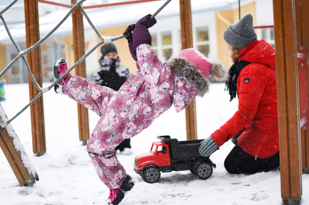 Pieni lapsi kiipeilee telineessä talvella päiväkodin pihalla.