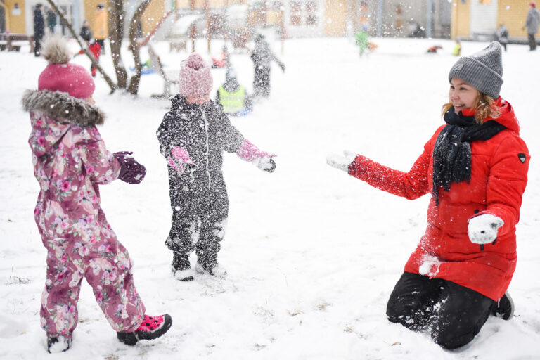 Aikuinen ja kaksi lasta leikkivät lumessa.