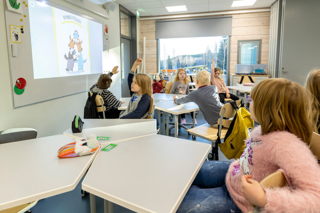 Koululuokka täynnä oppilaita, jotka viittaavat ahkerasti.