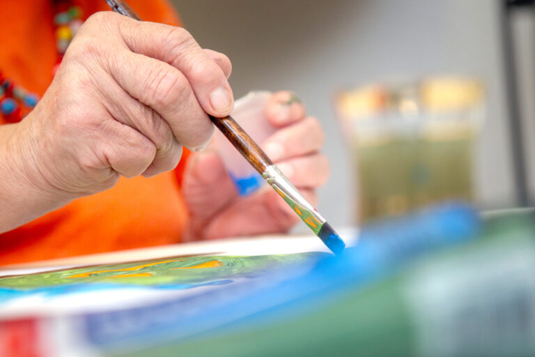 Kuvassa sivellin kädessä henkilö maalaa paperille.