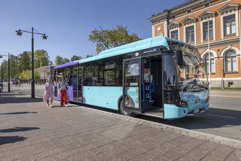 Linja-auto kaupungintalon edustalla ja kaksi naishenkilöä kävelee bussista ulos.