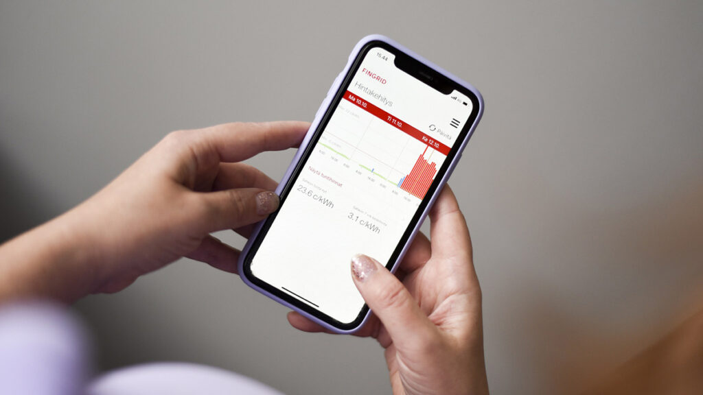 Naishenkilön käsissä älypuhelin, jossa energiankulutuksen näyttävä sovellus.
