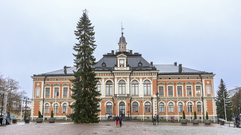 Taustalla Kuopion kaupungintalo, jonka edessä perinteinen Kuopion torin joulukuusi pystytettynä.