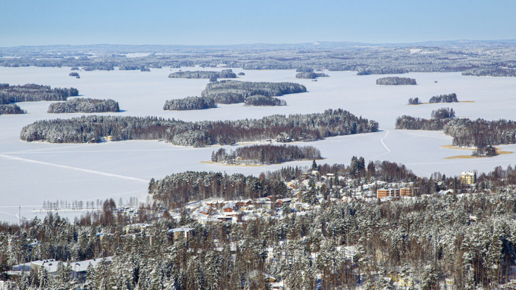 Talvinen Kallavesi-maisema, jossa edessä metsää ja taustalla saaria ja sinistä taivasta.