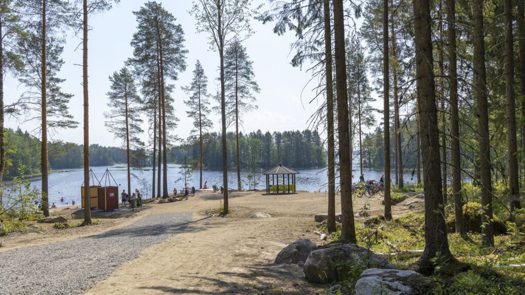 Uimaranta takana, pukukopit ja maja hiekalla. Uimareita kuvassa kauempaa kuvattuina.
