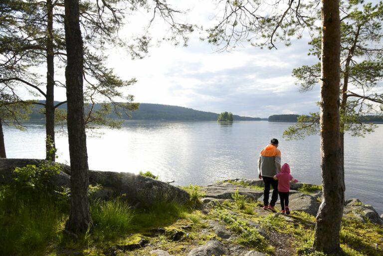 Järven ranta, jonka edustalla aikuinen ja lapsi.