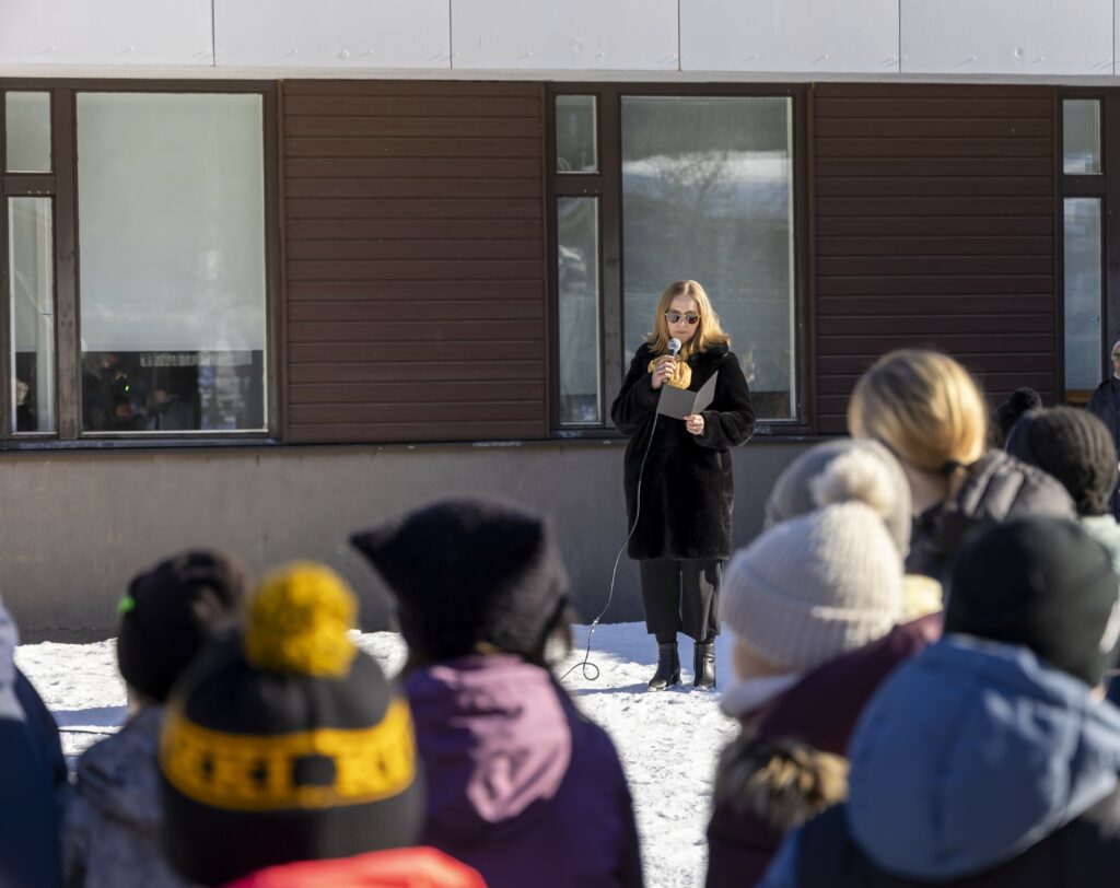 Rehtori pitää juhlapuhetta ulkona, koulun edustalla keväisenä pakkaspäivänä.