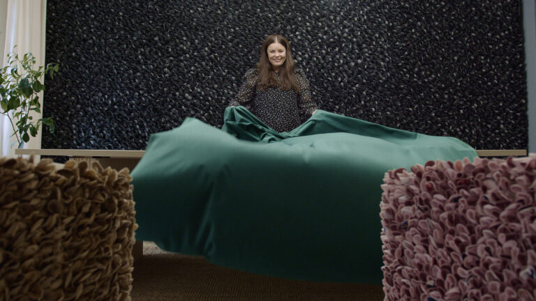 A woman is spreading a large green fabric over a big table.
